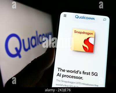 Person mit Mobiltelefon und Webseite des US-Halbleiterunternehmens Qualcomm Incorporated auf dem Bildschirm mit Logo. Konzentrieren Sie sich auf die Mitte des Telefondisplays. Stockfoto