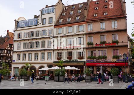 Menschen sitzen, zu Fuß, vor Gebäuden mit Architektur unverwechselbar der Region Elsass, Place Gutenberg, Straßburg, Frankreich. Stockfoto