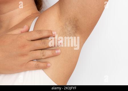 Frau berühren haarige Achselhöhlen mit Nahaufnahme der Hand, Freiraum für Kopien, beigefarbener Hintergrund. Angehobener Arm mit Achselhaaren. Weiblicher Beauty-Trend, Freiheit, Feminismus Stockfoto