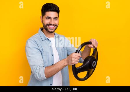 Foto von jungen lächelnden selbstbewussten Kerl spielen Videospiel Autofahren Test isoliert auf hellgelben Hintergrund Stockfoto