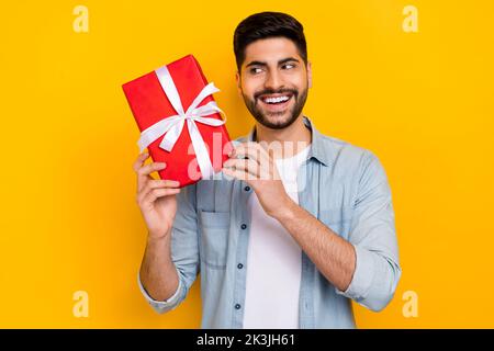 Foto-Porträt von fröhlichen latein jungen Kerl halten erraten wünschenswert Geschenk tragen trendige Denim-Kleidungsstück auf gelbem Hintergrund isoliert Stockfoto