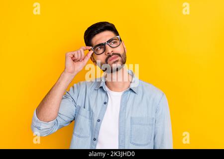 Porträt eines jungen, nachdenklichen Geschäftsmannes in einer Brille, die ernsthaft auf einem hellgelben Hintergrund träumt Stockfoto