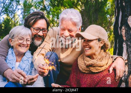 Familiengruppe Feiern und Spaß haben zusammen mit Feuerfunkern in den Wäldern Natur im Freien. Ältere und Erwachsene Menschen im gemischten Alter lächeln und lachen umarmt Stockfoto