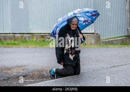 PERECHYN, UKRAINE - 25. SEPTEMBER 2022 - Eine ältere Frau mit einem Regenschirm kniet nieder, um dem Oberleutnant Armen Petrosian, 50, WHO, ihren letzten Respekt zu erweisen Stockfoto