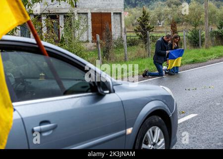 PERECHYN, UKRAINE - 25. SEPTEMBER 2022 - Ein Mann und eine Frau mit ukrainischer Flagge knieten nieder, um dem Oberleutnant Armen Petrosia ihren letzten Respekt zu erweisen Stockfoto