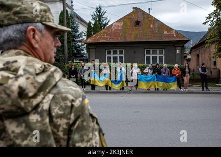 PERECHYN, UKRAINE - 25. SEPTEMBER 2022 - Menschen halten ukrainische Flaggen in der Hand, um den Konvoi mit dem Leichnam von Oberleutnant Armen Petrosian, 50, WHO, zu begrüßen Stockfoto