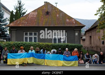 PERECHYN, UKRAINE - 25. SEPTEMBER 2022 - Menschen mit ukrainischen Flaggen knien, während die Autokolonne mit dem Leichnam von Oberleutnant Armen Petrosian, 50, Stockfoto