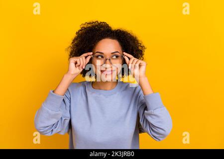 Portrait von positiven charmanten Mädchen Hände berühren Gläser schauen interessiert leeren Raum auf gelbem Hintergrund isoliert Stockfoto