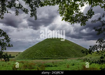silbury Hill in der Nähe von avebury wiltshire durch einen Rahmen von Bäumen mit dramatischen Wolken gesehen Stockfoto