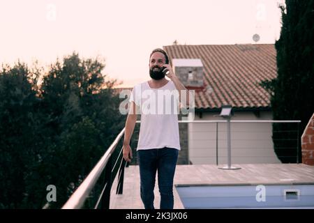 Ein junger, gutaussehender Mann freute sich, einen lustigen Telefonanruf zu haben, während er in seinem Haus ging Stockfoto