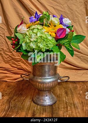 Ein schöner, farbenfroher Blumenstrauß. In einem antiken Champagnerhalter. Auf einem Holztisch mit hellbraunem Hintergrund. Stockfoto