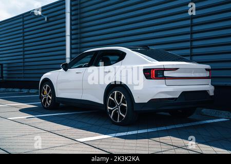 Eine Seitenrückansicht des Snow White Polestar 2, der im Schatten vor dem Metallgebäude geparkt ist Stockfoto