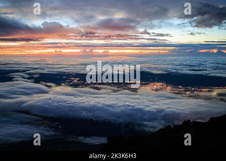 Blick auf Wolken und Lichter der Stadt vom Gipfel des Mt. Fuji vor Sonnenaufgang Stockfoto