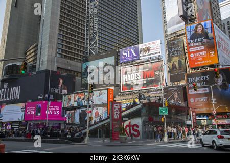 Die Leute stehen an, um ermäßigte Theaterkarten am Times Square mit Werbetafeln zu kaufen, die im Hintergrund am Broadway in New York City spielen. Stockfoto