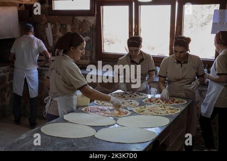 Mardin, Türkei. 26. September 2022. Assyrische Frauen sahen, wie sie Pizza bei Kafro's Pizza, Mardin, zubereiteten. Im Dorf Elbegendi im Bezirk Midyat von Mardin gibt es einen Pizzaladen namens Kafro's Pizza. Der Name der Pizzeria stammt aus dem Dorf Elbegendi, wo Assyrer leben, auf dem Berg Bagok. Der Pizzaladen, dessen Besitzer und Mitarbeiter assyrisch sind, empfängt aufgrund seiner Lage im Dorf und seiner köstlichen Pizzen jeden Tag Dutzende von Kunden. Nail Demir, der Besitzer des Ortes, lernte während seines Lebens in Europa Pizza zu machen und beschloss vor 10 Jahren, Kafro's Pizza im vi zu eröffnen Stockfoto