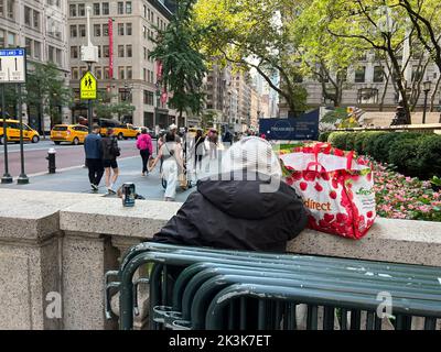 Obdachlose Frau blickt von der Terrasse der New York Public Library in der 42. Street auf die 5. Avenue. Stockfoto