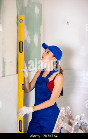 Attraktive junge Bauherrin in Arbeitskleidung gekleidet, die den Füllstand im Renovierungsprozess überprüft Stockfoto