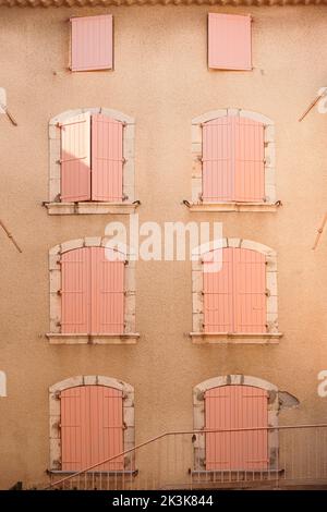 Viele rosafarbene Fensterläden aus Holz an pastellorange gestrichenen Wänden. Geschlossene Fenster im europäischen Stil mit Zierrahmen an der Gebäudefassade Stockfoto