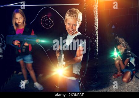 Positiver Teenager Junge steht mit Laserpistole im dunklen Lasertag Raum während des Spiels mit Freunden Stockfoto