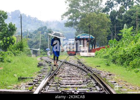 Mann, der an einem regnerischen Tag auf der Bahn läuft. Er hat einen Regenschirm in der Hand. Mann mit Regenschirm auf der Bahn, wartet auf neue Abenteuer und Reisen. Stockfoto