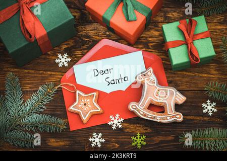 Babybrief an den Weihnachtsmann, roter Umschlag mit einer Postkarte mit handgeschriebenen Worten, lieber Weihnachtsmann, Weihnachtsdekorationen, Geschenke, Lebkuchen, Frohe Stockfoto