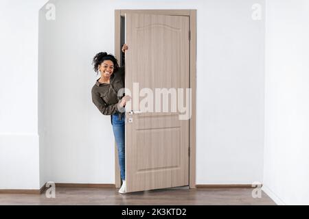 Fröhliche Schwarze Frau, Die Die Tür Öffnet, Lächelt Im Neuen Zuhause Stockfoto