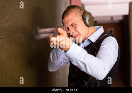 Fokussierter Mann, der die Schrotflinte auf das Ziel im Schießstand anvisiert Stockfoto