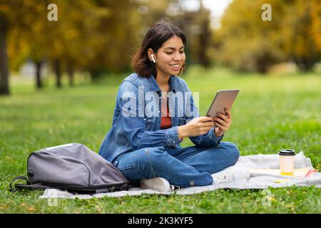 Junge Lächelnde Arabische Frau, Die Sich Mit Einem Digitalen Tablet Im Park Entspannt Stockfoto