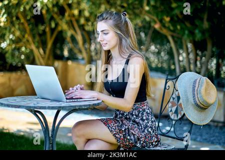 Porträt einer jungen kaukasischen Frau, die mit einem Laptop im Garten posiert und im Internet nach Informationen sucht. Lifestyle-Konzept. Stockfoto