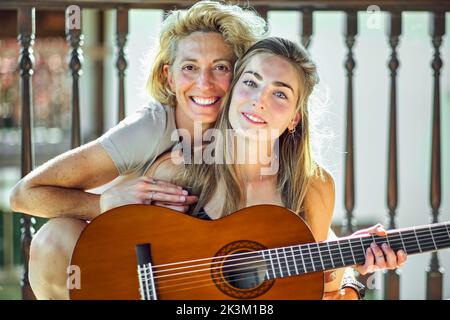 Porträt einer jungen kaukasischen Frau und ihrer schönen Tochter mit einer akustischen Gitarre auf der Veranda eines Landhauses. Lifestyle-Konzept. Stockfoto