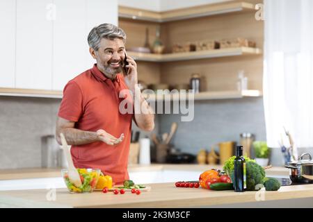 Fröhlicher grauhaariger Mann, der seine Freunde zum Abendessen einlud Stockfoto
