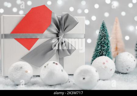 Weißer roter Anhänger auf einer Geschenkbox vor dem Hintergrund des Weihnachtsdekor. Weihnachten und Neujahr Rabatte und Verkäufe. Stockfoto