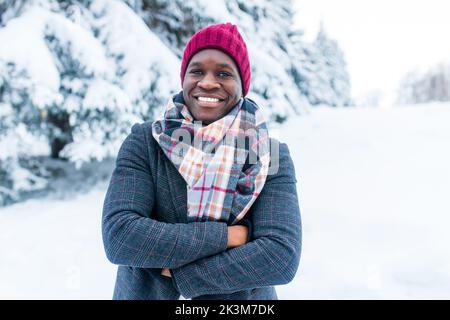 afroamerikanischer Handsom-Mann in rotem Hut und stilvollem karierten Mantel Blick auf die Kamera mit toothy schneeweißen Lächeln im Freien im Park Stockfoto