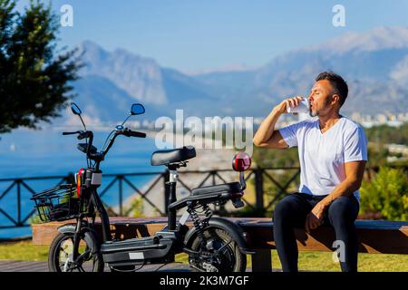 Alter Mann gut im Freien mit Öko-Scooter genießen Morgen und Kaffee trinken Stockfoto