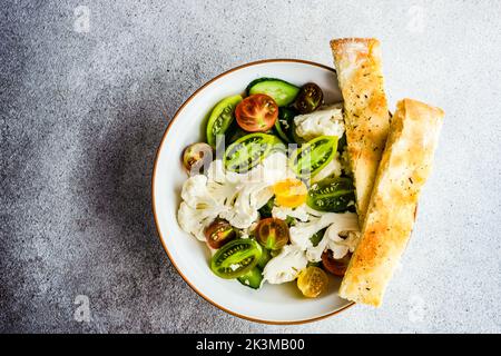 Gesunder Gemüsesalat in der Schüssel und frisch gebackenes Focaccia-Brot auf einem Betontisch Stockfoto