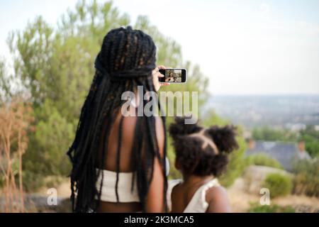 Weicher Fokus von anonymer afroamerikanischer Mutter und Tochter, die zusammen Selfie über das Smartphone machen, während sie den Sommerwochenende in der Natur verbringen Stockfoto