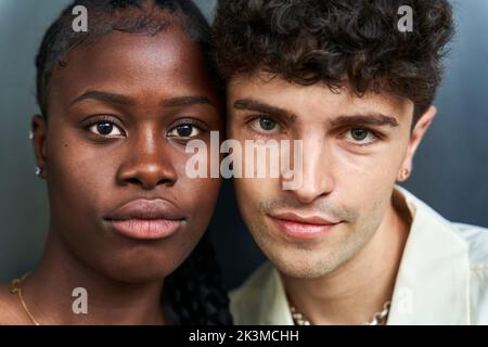 Headshot von jungen, vielfältigen Frauen und Männern mit lockigen Haaren, die Gesichter berühren, während sie die Kamera auf grauem Hintergrund betrachten Stockfoto