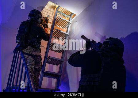 Rückansicht von nicht erkennbaren männlichen Soldaten in Schutzkleidung und Helm, die auf der Treppe stehen und mit Gewehren zielen Stockfoto