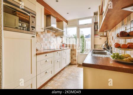 Gut organisierte kleine Wohnküche mit Waschbecken unter dem Fenster Und helle Möbel mit Herd und Kühlschrank in städtischen Wohnung Stockfoto