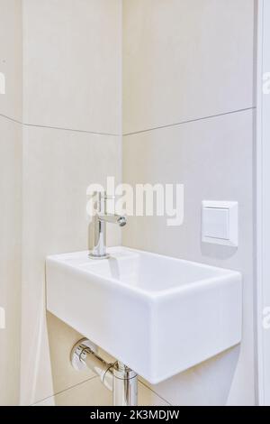 Weißes Keramikwaschbecken mit glänzendem Chrom-Wasserhahn an beigefarbener Wand in der Toilette Stockfoto
