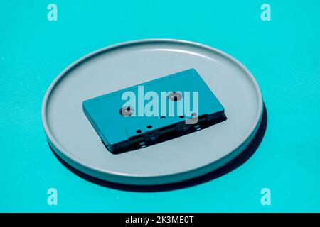 Hoher Winkel der altmodischen Kompaktkassette auf runder Platte auf blauem Hintergrund im Studio platziert Stockfoto