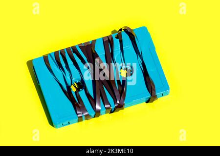 Von oben aus blaue altmodische Audiokassette mit verworrenem Magnetband, das im Studio auf einem leuchtend gelben Hintergrund platziert wurde Stockfoto