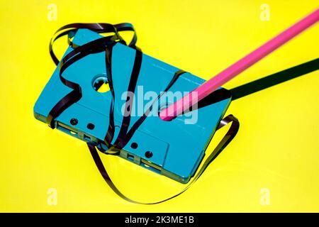Hoher Winkel der blauen Retro-Kassette mit unordentlichem Magnetband und Bleistift zum Zurückspulen auf gelbem Hintergrund im Studio platziert Stockfoto