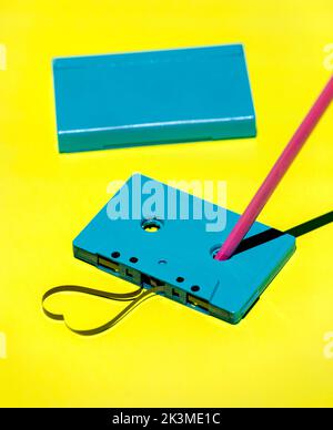 Hoher Winkel der blauen Retro-Kassette mit unordentlichem Magnetband und Bleistift zum Zurückspulen auf gelbem Hintergrund im Studio platziert Stockfoto