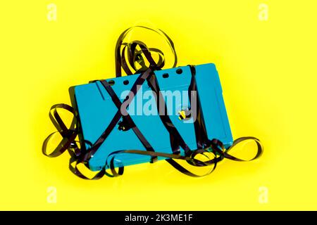 Von oben aus blaue altmodische Audiokassette mit verworrenem Magnetband, das im Studio auf einem leuchtend gelben Hintergrund platziert wurde Stockfoto