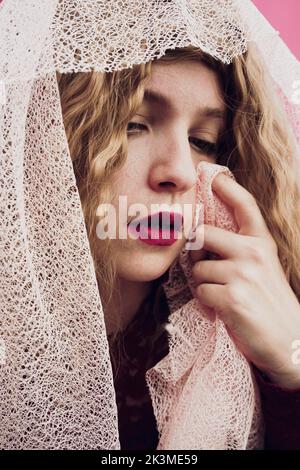 Junge traurige Frau mit roten Lippen weinen und Tränen wischen mit Schleier über den Kopf im Studio Stockfoto
