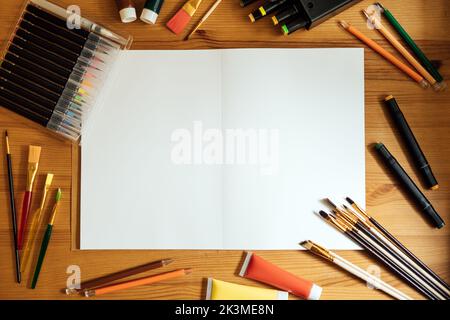 Kreativer Künstler mockup Arbeitsplatz auf Holztisch . Flachlage, Draufsicht mit leerem Skizzenbuch mit Copyspace, Bleistiften, Pinsel und Farben. Kunst Stockfoto