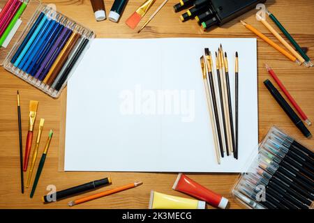 Kreativer Künstler mockup Arbeitsplatz auf Holztisch . Flachlage, Draufsicht mit leerem Skizzenbuch mit Copyspace, Bleistiften, Pinsel und Farben. Kunst Stockfoto