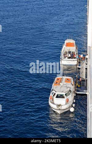 Mykonos, Griechenland - Mai 2022: Kleine Motorboote, die Passagiere eines vor der griechischen Insel Mykonos vor der Küste festgefahrenen Kreuzfahrtschiffs abholen Stockfoto