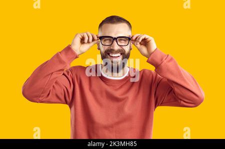 Fröhlicher, fröhlicher bärtiger Mann in einer Brille, der auf gelbem Hintergrund steht und lacht Stockfoto